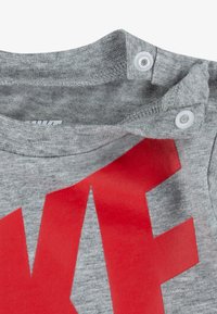 Grå bomull T-skjorte med rund hals, med rød Nike-logo trykk og to trykknapper ved kragen for lukking.