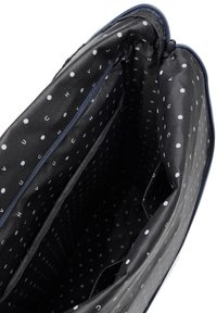 Schwarze Stofftasche mit einem weißen Punktmuster im Inneren. Verfügt über Reißverschlussfächer und glattes, strukturiertes Futter.