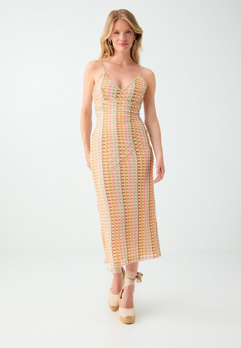 Femme portant une robe midi sans manches à motifs avec fines bretelles et des espadrilles compensées beiges avec liens à la cheville, debout sur un fond blanc.