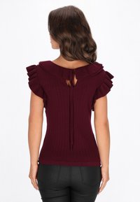 Top tricotat burgund cu model cu dungi, având un guler volanat, închidere cu fundă la spate și mâneci scurte cu volane. Textură fină și croială ajustată.