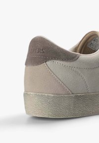 Zapatillas de ante en gris y beige, con suela de goma texturizada y un trasero cosido con detalle de marca. Forma redondeada, diseño casual.