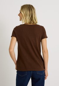 Camiseta corta de manga corta en color marrón con bordes enrollados, escote redondo y tela suave; combinada con vaqueros azul oscuro. Diseño minimalista, sin patrones ni acentos.