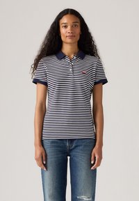 Randig polo skjorta i marinblått och vitt med kort krage och ärmar. Har en liten röd Levi's-logotyp på vänster bröst. Bärs med blå jeans.