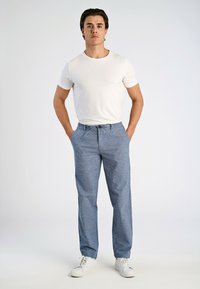 Jasnoszara koszulka zestawiona z niebieskimi, teksturowanymi spodniami dresowymi z elastycznym pasem i sznurkiem, noszona z białymi trampkami.