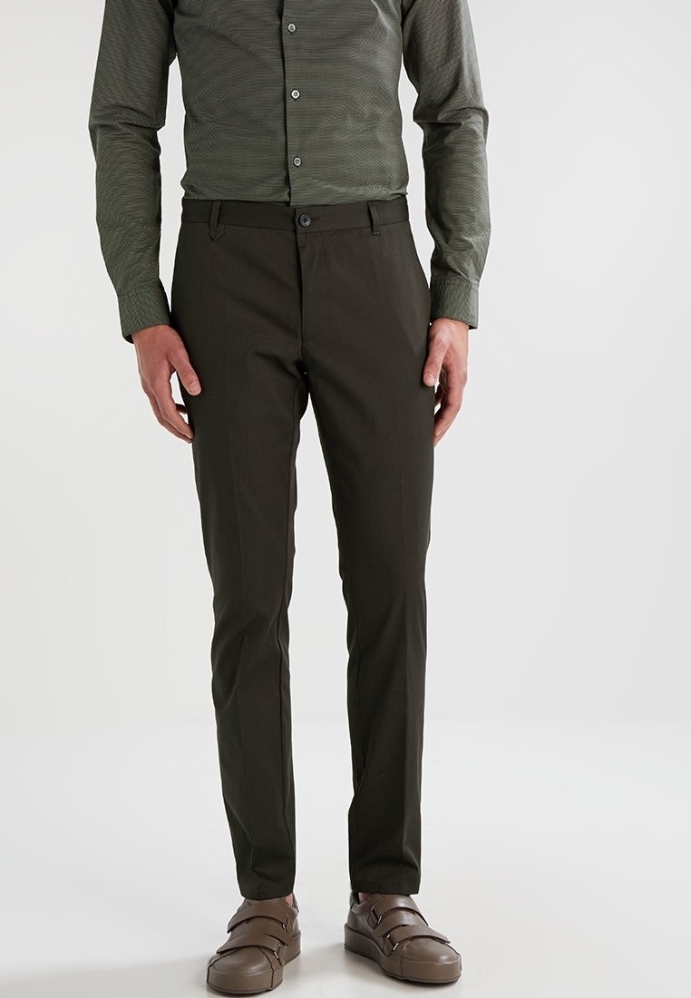 Donkergroene broeken met een slim fit, gemaakt van gladde stof. Voorzien van een knoopsluiting en zijzakken, gecombineerd met bruine, platte sandalen.
