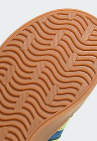 Rubberen schoenzool met een golvende textuur, in een lichtoranje kleur en gedetailleerde grippatronen. Inclusief een gegolfde rand.