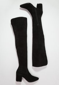 Yli polven ulottuvat mustat mokkanahkabootsit, joissa on paksu korko, sivuvetoketju ja sileä pinta. Tyylikkäästi muotoiltu design.