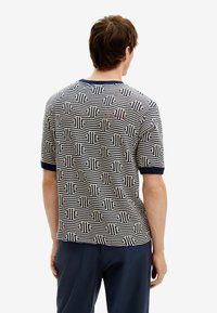 Krátký rukáv pletená vzorovaná košile s geometrickými liniemi v námořnické modři na krémovém pozadí, s žebrovaným námořnickým límcem a manžetami.