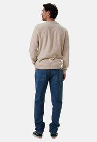 Sweatshirt beige clair avec un col rond, des poignets et un ourlet côtelés. Associé à un jean en denim bleu et des chaussures de skate noires. Vue de l'arrière.