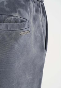Grijze sweatpants met een gestructureerde stof, zijzak en een metalen logo-plaat vlakbij de zak voor branding.