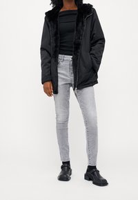 Černá zateplená bunda s umělou kožešinou, spárovaná s černým žebrovaným topem, světle šedými skinny jeans a černými masivními botami.