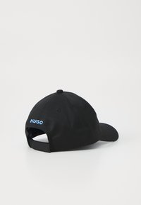 Musternaga spordikiiver, millel on kaardus visiiir, valmistatud puuvillast. Seljaosas on sinine brodeeritud "HUGO" logo ja reguleeritav rihm.