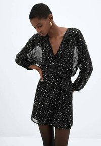 Abito avvolgente nero con maniche lunghe e ampie, caratterizzato da un motivo a macchie bianche. Realizzato in tessuto leggero e trasparente. Legato in vita.