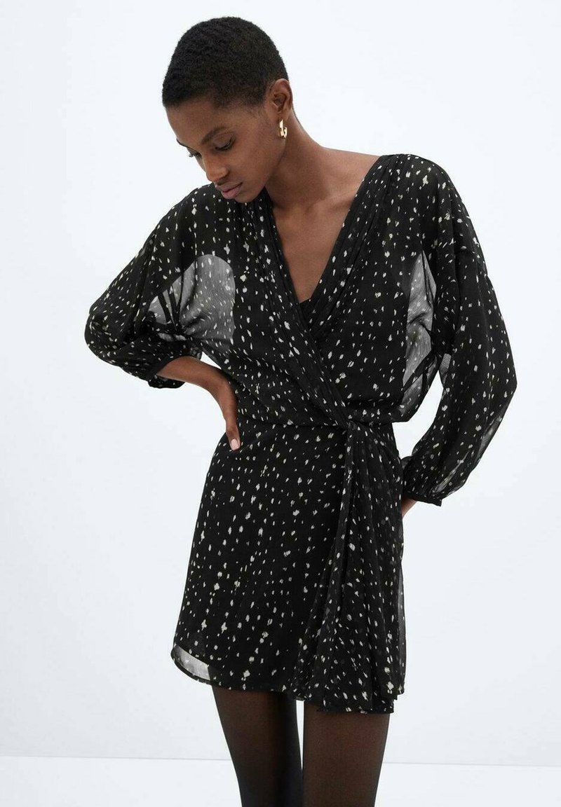 Abito avvolgente nero con maniche lunghe e ampie, caratterizzato da un motivo a macchie bianche. Realizzato in tessuto leggero e trasparente. Legato in vita.