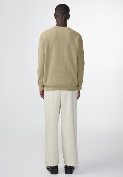 Beige gebreide trui met een ronde hals, lange mouwen en ribbelstructuur, gecombineerd met losse crème broek en zwarte schoenen.