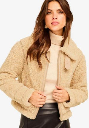 Beež shearling jakk, millel on tõmblukk ees, kraega disain ja siledad pruuni toonid. Omab tekstureeritud kangast ja lõdva lõikega.