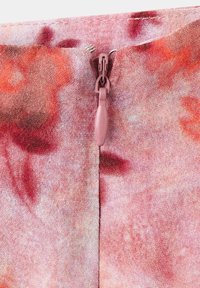 Gros plan d'une fermeture éclair rose partiellement ouverte sur un tissu à motifs tie-dye rouges et oranges.