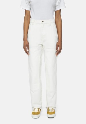 Pantalones de mezclilla blanca con un corte recto, que presentan un cierre de botón y bolsillos laterales, combinados con zapatillas de ante amarillas.