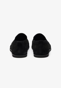 Svarte semskede slip-on sko med rund tå og lavprofil svart gummisåle. Myk tekstur og minimal sømdetalj bak.