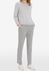 Maglione grigio chiaro a righe in morbido tessuto con collo tondo; abbinato a pantaloni grigio chiaro su misura e sneakers bianche. Vestibilità rilassata e design minimale.