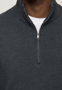 Grijze geribde gebreide pullover met een staande kraag en een zilveren rits, met een schone, textuurachtige oppervlakte en een witte binnenlaag die zichtbaar is bij de nek.