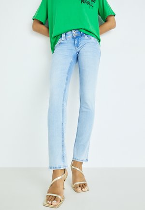 Light blue denim jeans with a slim fit and subtle faded texture, paired with gold strappy sandals and a green oversized T-shirt.
