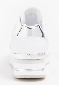 Bílá teniska s hladkým koženým svrškem, polstrovaným límcem a lesklým chromovaným akcentem na patě. Má texturovanou gumovou podrážku.