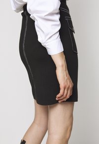 Schwarzer Strickrock mit weißer Naht, ausgestattet mit einer Seitentasche und einem schlanken Schnitt. Kombiniert mit einem weißen Langarmshirt.