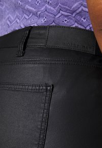 Pantalons en faux cuir noir avec une texture lisse, comportant une poche arrière et une étiquette embossée "NOISY MAY" au niveau de la taille.