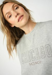 Grauer Sweatshirt mit gesticktem "CHICAGO" und "MOS MOSH" in kontrastierenden Farben. Weicher Stoff mit Rundhalsausschnitt und subtiler Textur.