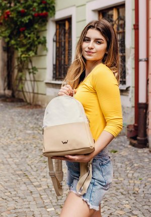 Beige a krémový dvoubarevný batoh s hladkou texturou, zaobleným tvarem a přední kapsou. Obsahuje nastavitelné popruhy a detail s logem.