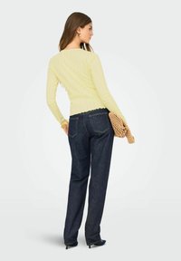 Ljusgulfärgad ribbad stickad topp med lång ärm och en scallopdetalj i nederkant, parat med marinblå vida jeans, samt en texturerad handväska.