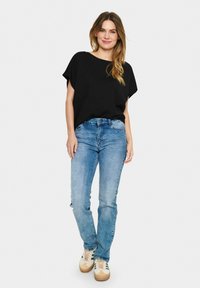 Sort kortærmet top sammen med lyseblå jeans. Modellen har casual sko med et beige og grønt mønster på. Enkel, afslappet pasform.