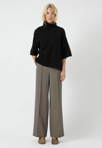 Czarny, dzianinowy, oversize'owy sweter z wysokim kołnierzem i krótkimi rękawami, połączony z beżowymi spodniami o wysokim stanie i szerokich nogawkach oraz brązowymi sandałami na obcasie.