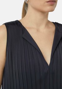 Abito nero plissettato con profonda scollatura a V e design senza maniche. Il tessuto ha una consistenza liscia e sottile con righe verticali.