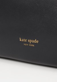 Black leather bag with textured surface, featuring a gold embossed logo "kate spade NEW YORK" at the bottom.