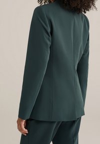 Mörkgrön skräddarsydd kavaj med en elegant design, mjuk textur, strukturerade axlar och en enda vent bak.