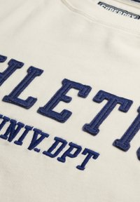 Sudadera blanca con grandes letras bordadas en azul marino que dicen "ATHLETIC" y "UNIV.DPT", con cuello redondo y tejido texturizado.