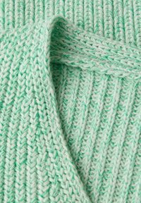 Gros plan sur un tissu en tricot épais et doux de couleur vert menthe avec une texture côtelée et des couches pliées créant des formes courbes.
