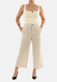 Pantaloni beige a gamba larga con righe verticali, dotati di chiusura a bottone e tasche laterali. Abbinati a un top crema a coste. Tacchi neri.