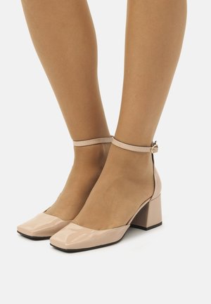 Scarpe in pelle lucida beige con tacco a blocco, punta quadrata, cinturino alla caviglia e una finitura liscia. Il tacco misura circa 4 cm.
