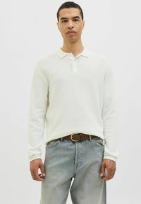 White long-sleeve polo shirt with a textured knit fabric, a soft collar, and a two-button placket, paired with light blue denim trousers.
