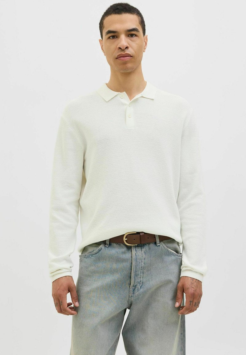 White long-sleeve polo shirt with a textured knit fabric, a soft collar, and a two-button placket, paired with light blue denim trousers.