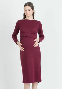 Těhotenské šaty v barvě burgundy, dlouhé rukávy, přiléhavý korzet s twistem vpředu, délka ke kolenům, elastický materiál, hladká textura.
