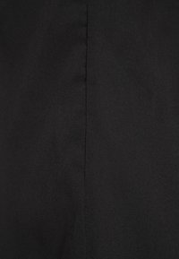 Tessuto nero con una texture liscia, caratterizzato da una cucitura verticale che scende al centro, creando un design minimalista.