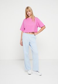 Ροζ cropped t-shirt με κοντά μανίκια σε συνδυασμό με ανοιχτό μπλε άνετο φόρμα παντελόνι. Η στολή έχει απλό σχεδιασμό και απαλό ύφασμα.