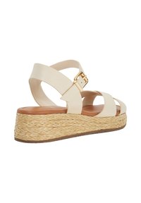 Beige leather wedge sandal with cross-strap design, gold buckle, and woven jute midsole. Smooth inner sole and textured outer sole.
