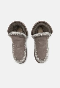 Pantofole in shearling grigio con design pieghevole, caratterizzate da un esterno testurizzato e una cucitura decorativa lungo i bordi. Fodera interna morbida.