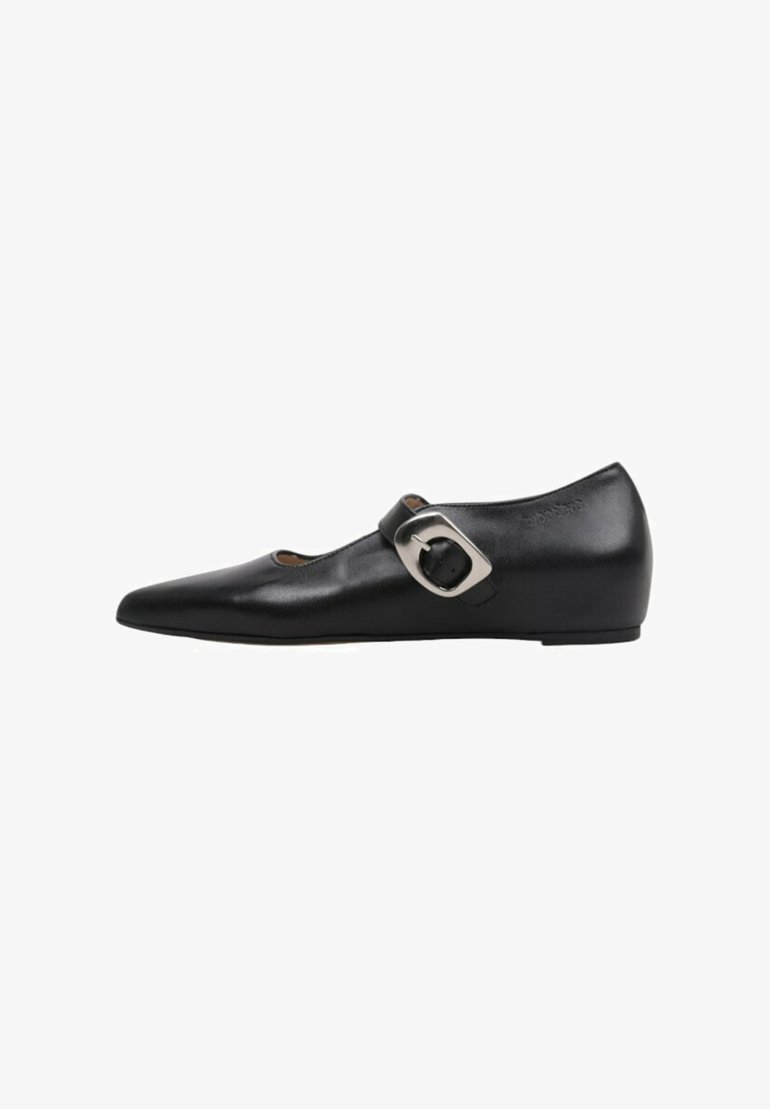 Zapato plano Mary Jane de cuero negro con puntera puntiaguda y gran hebilla plateada sobre fondo blanco.