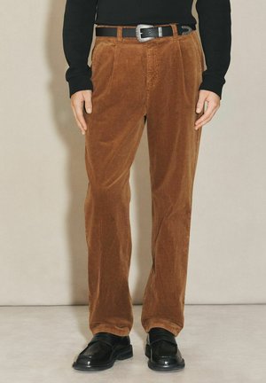 Brown corduroy trousers with a straight-leg design, featuring two front pockets, a black belt, and a textured finish. Black shoes complete the look.